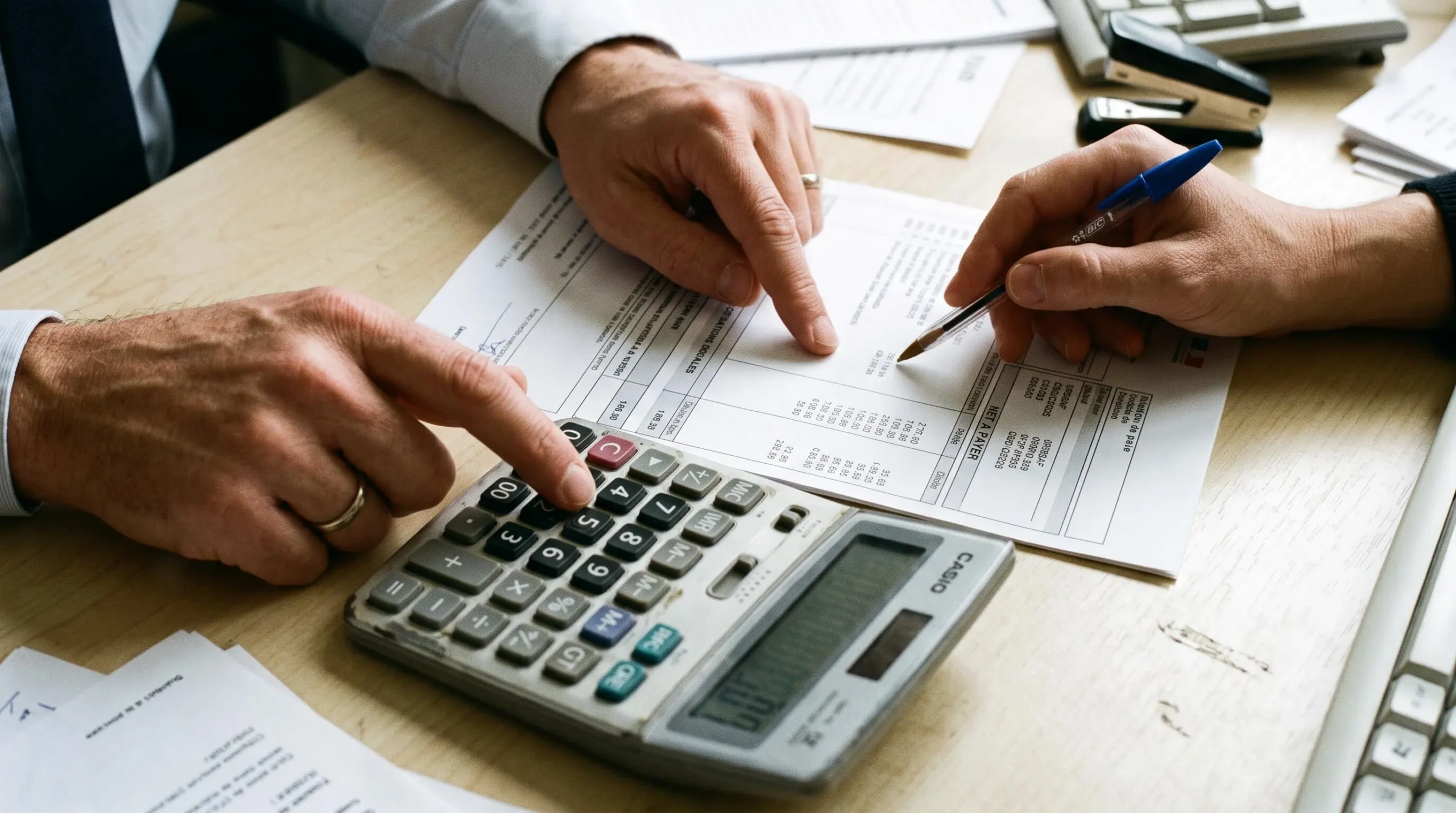 Mains d'un responsable RH vérifiant un bulletin de paie avec une calculatrice
